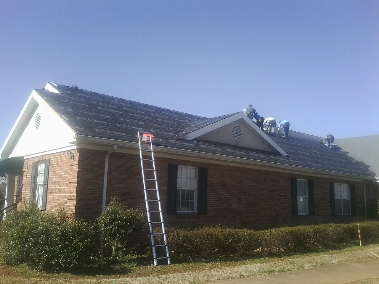 Crew tearing shingles off a brick ranch roof with a ladder set — Emergency Roof Repair work by our crew in Ayr