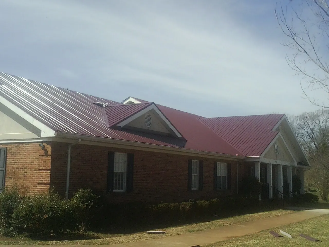 Red metal roof with gabled entries on a long brick building, from a Hail Damage Roof Repair job in Ayr