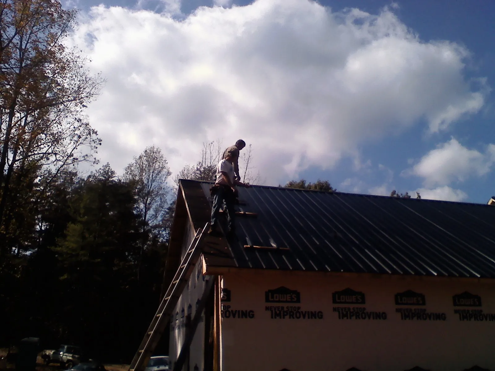 Roofer fastening dark metal panels high against a cloudy sky, from a Roof Inspection job in Ayr