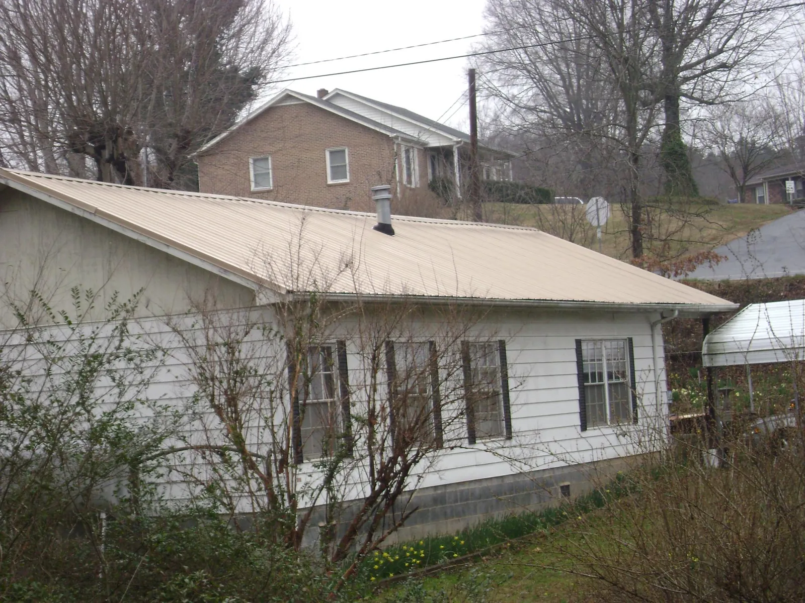 Tan metal roof on a white sided house set into a hillside — Commercial Roofing by Roofing Brothers in Ayr